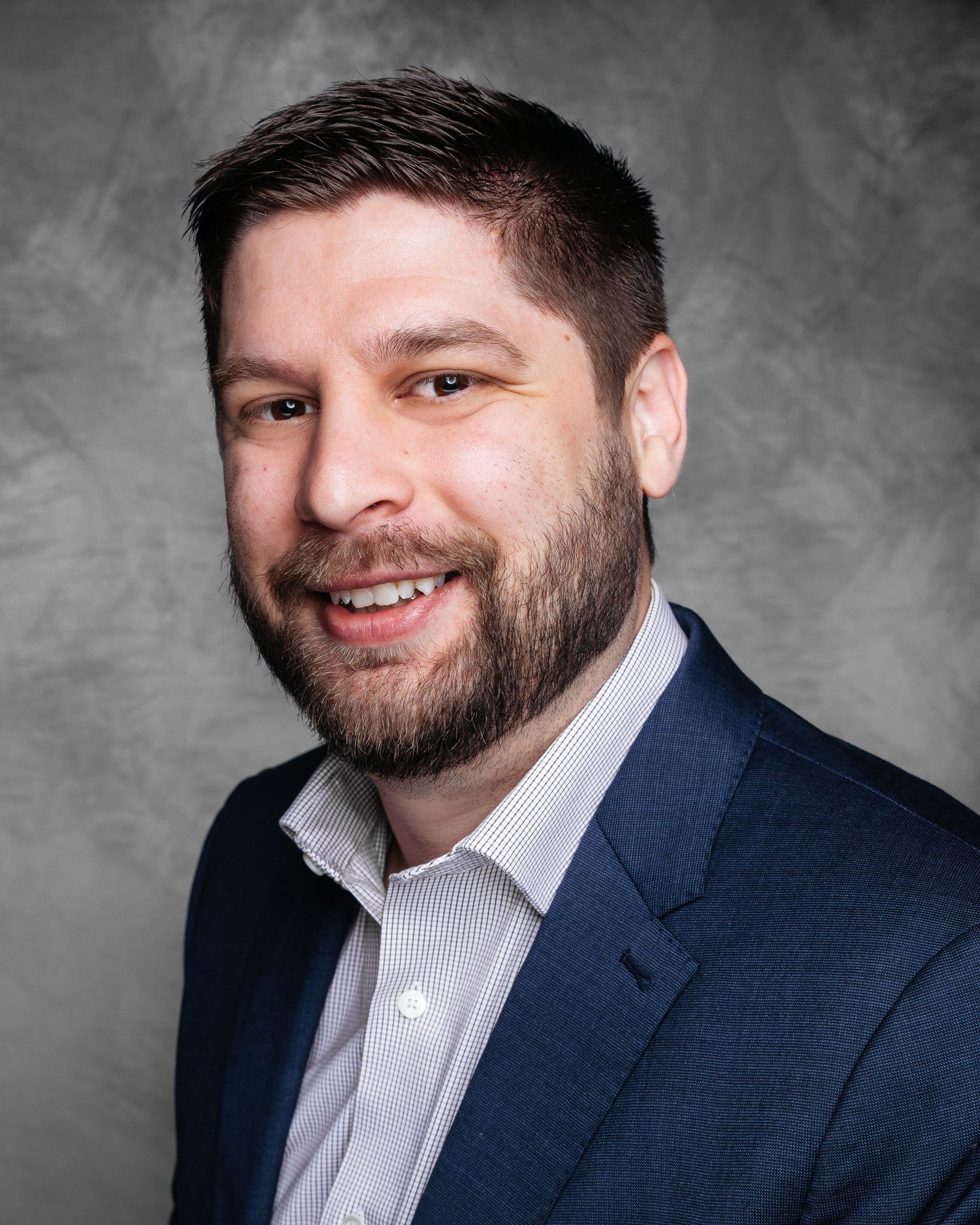 Professional headshots of person in navy suit and white shirt against gray background.
