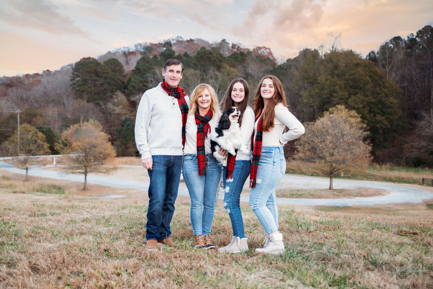 Group of friends in casual outfits pose together on a grassy hill during golden hour.