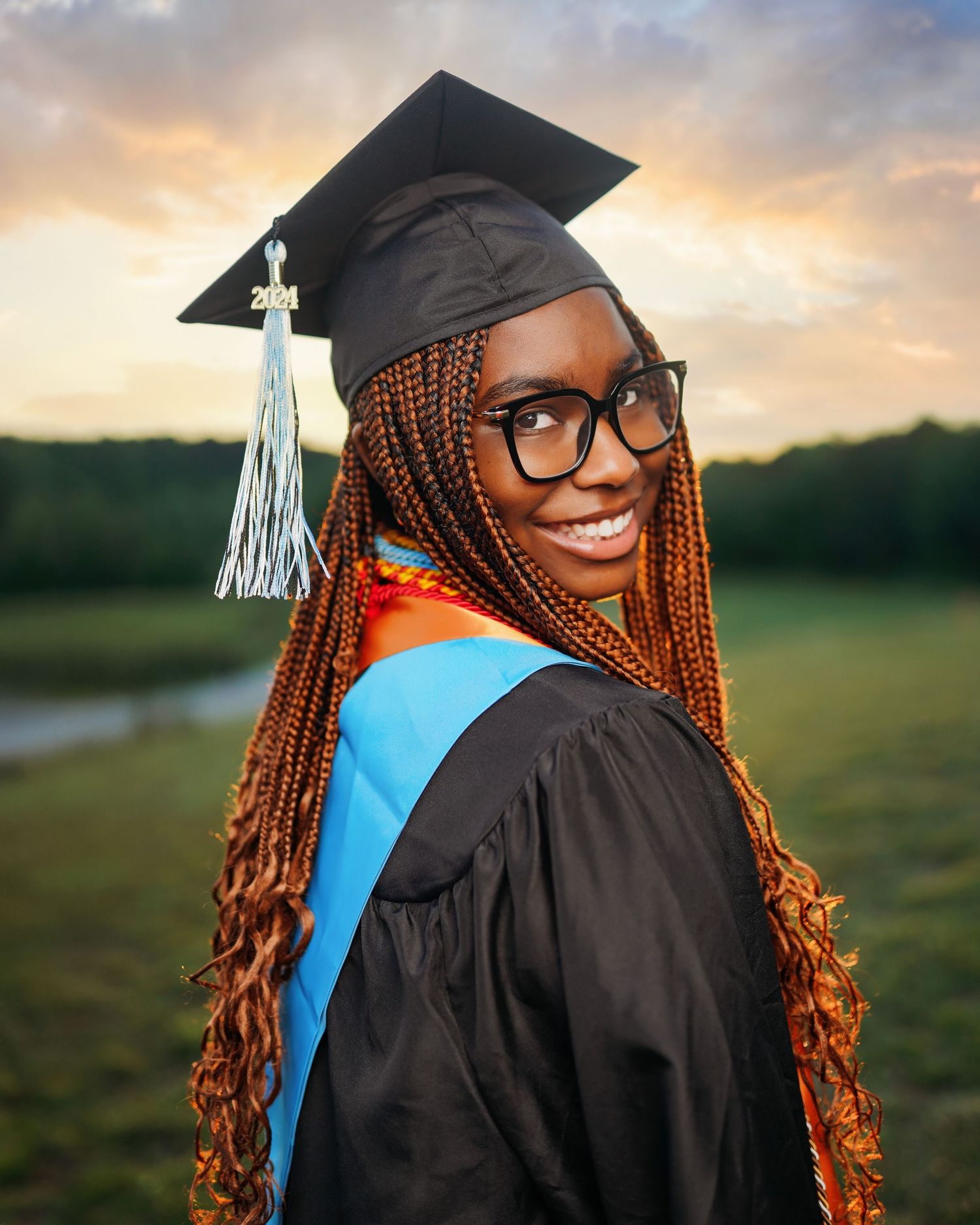 Graduation portraits at sunset with academic regalia against natural backdrop.