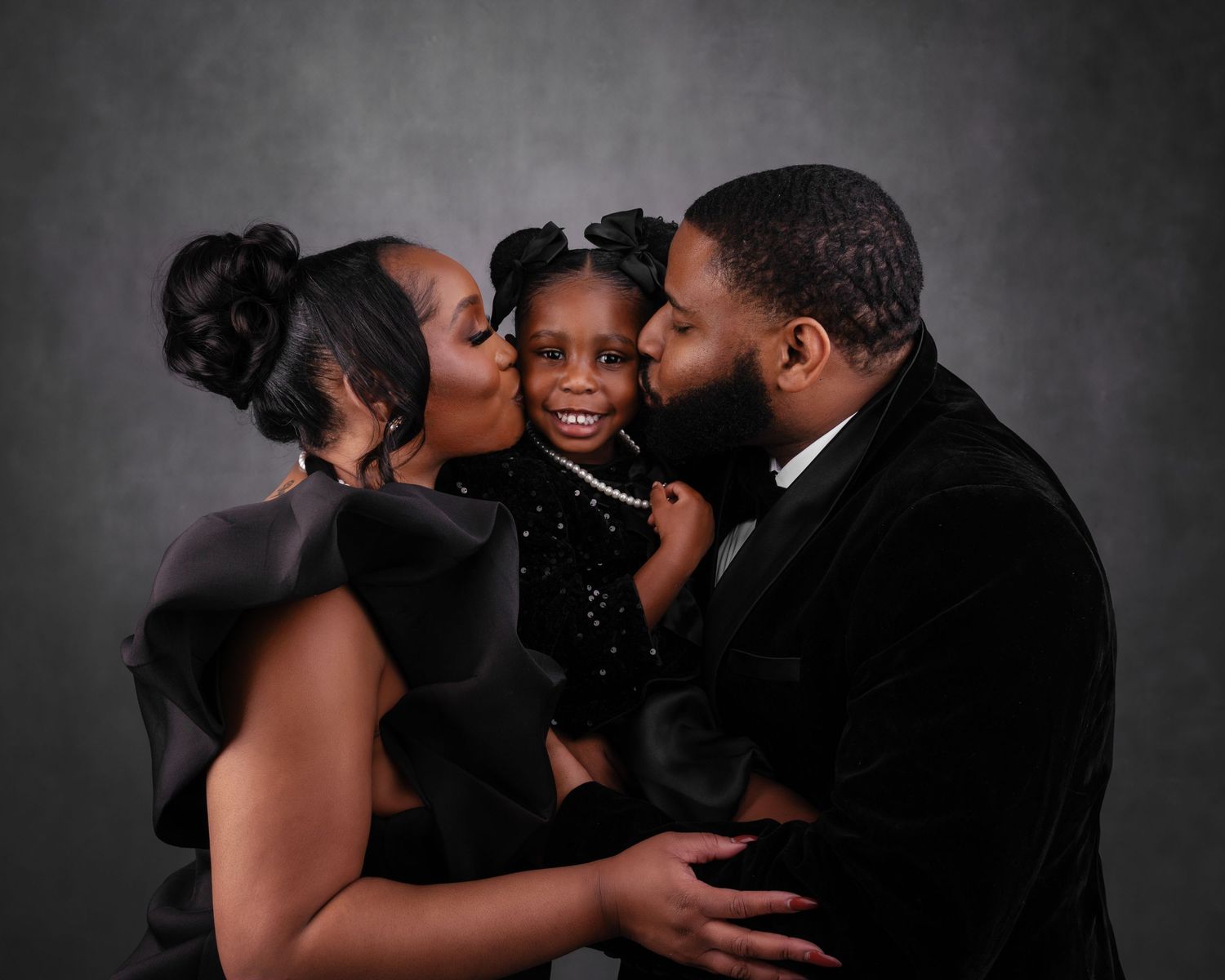 An elegant family portrait in formal black attire against a dark gray studio background.