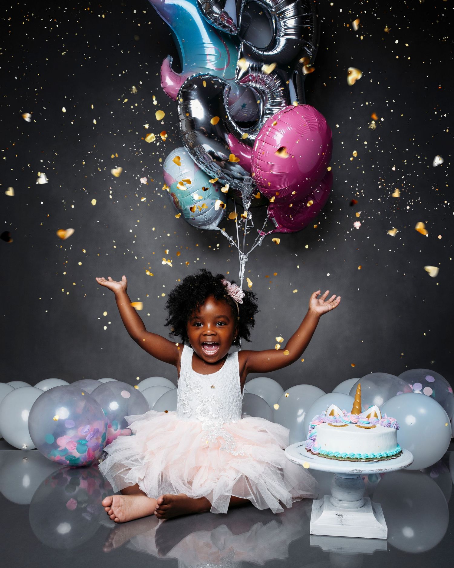 Celebratory cake smash photo session with balloons, confetti and pink tulle dress.