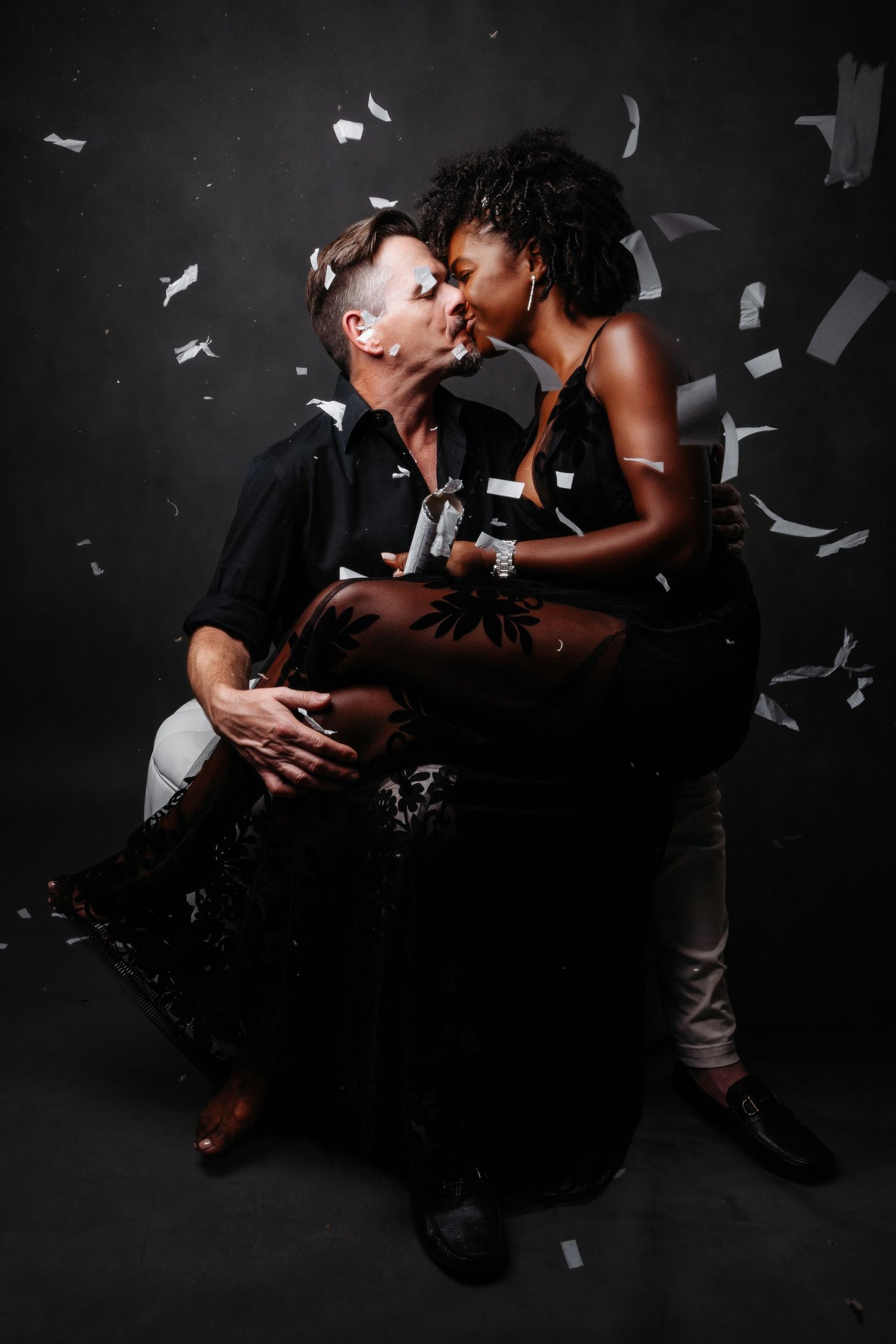 Romantic couple photoshoot with floating paper confetti against dark background.