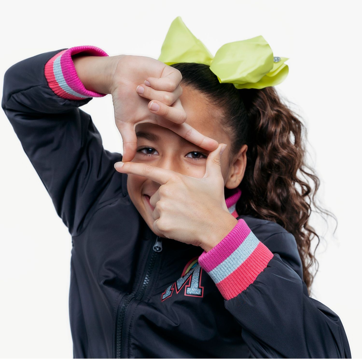 Person in black jacket and pink accents making playful gestures against white background.