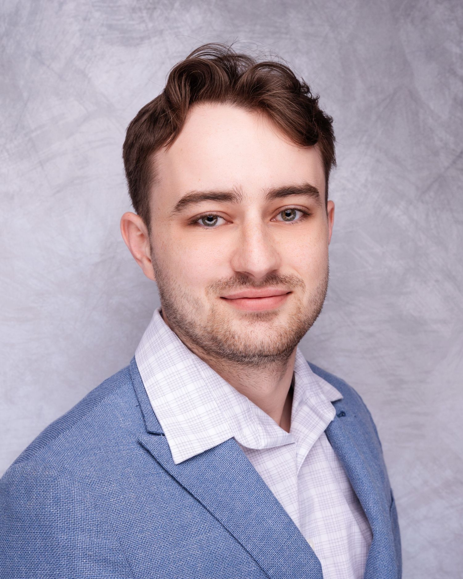 Business headshots of person in light blue suit and white shirt against textured backdrop.