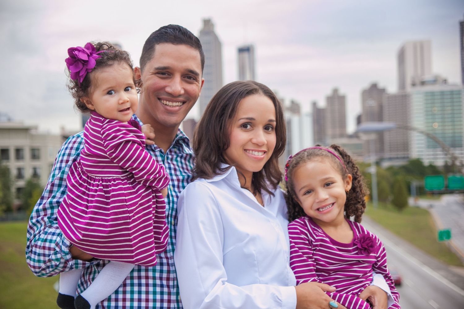 A family poses together against an urban skyline backdrop at sunset.