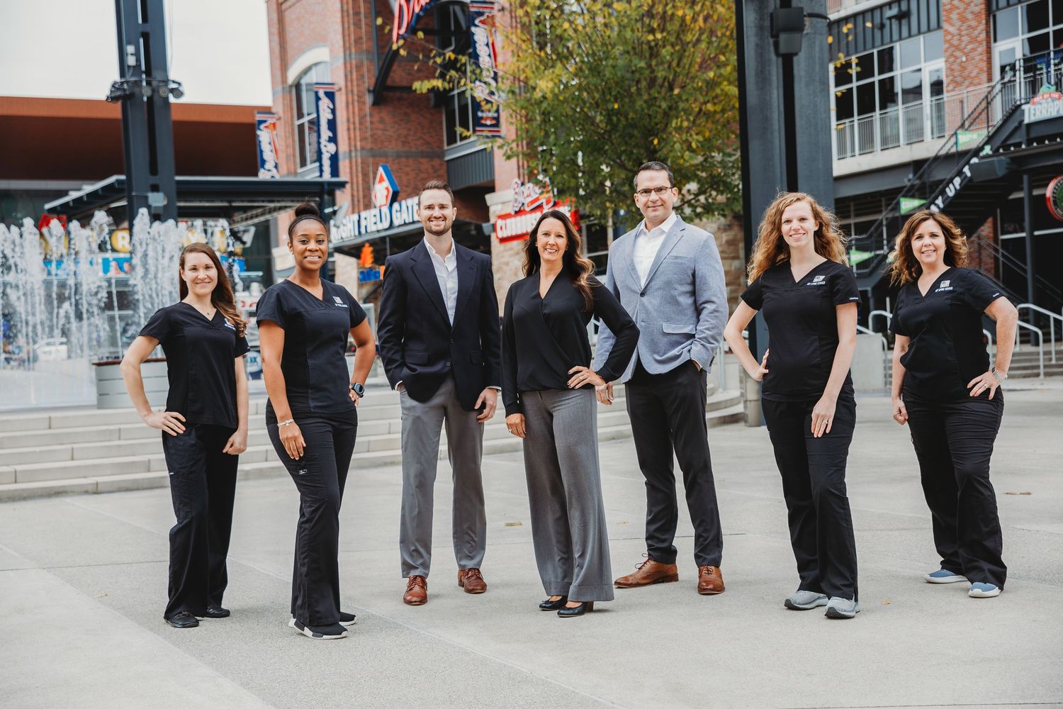 Professional team in coordinated business attire poses together outside modern building.