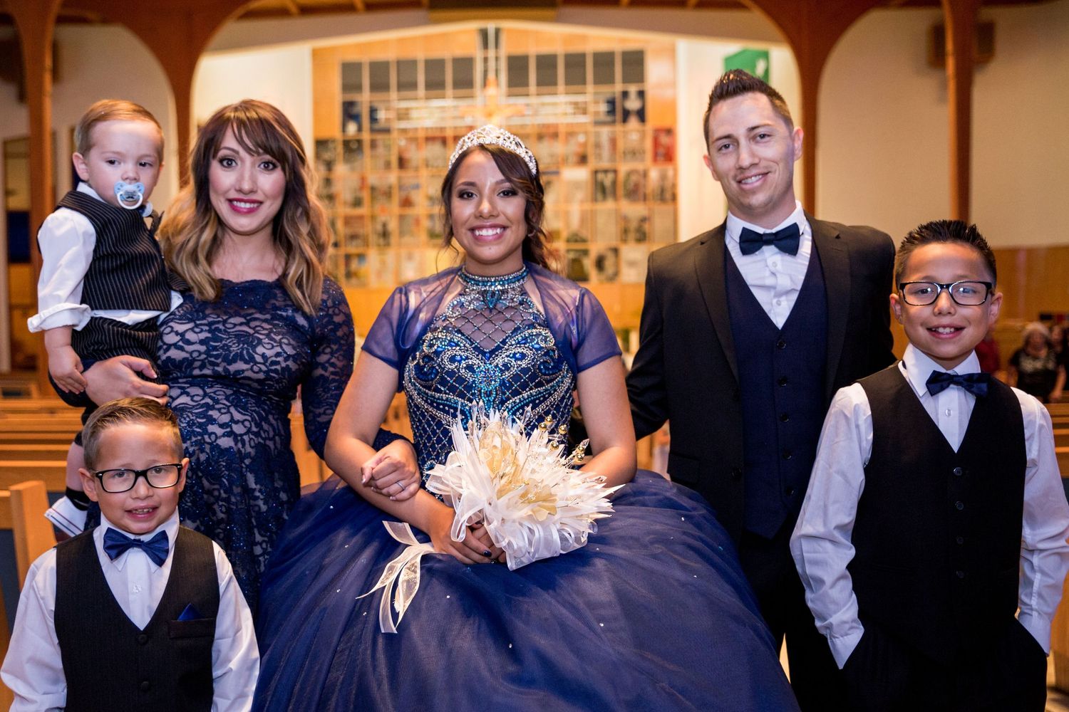 Wedding party lined up in navy blue dresses and black tuxedos at a formal event.