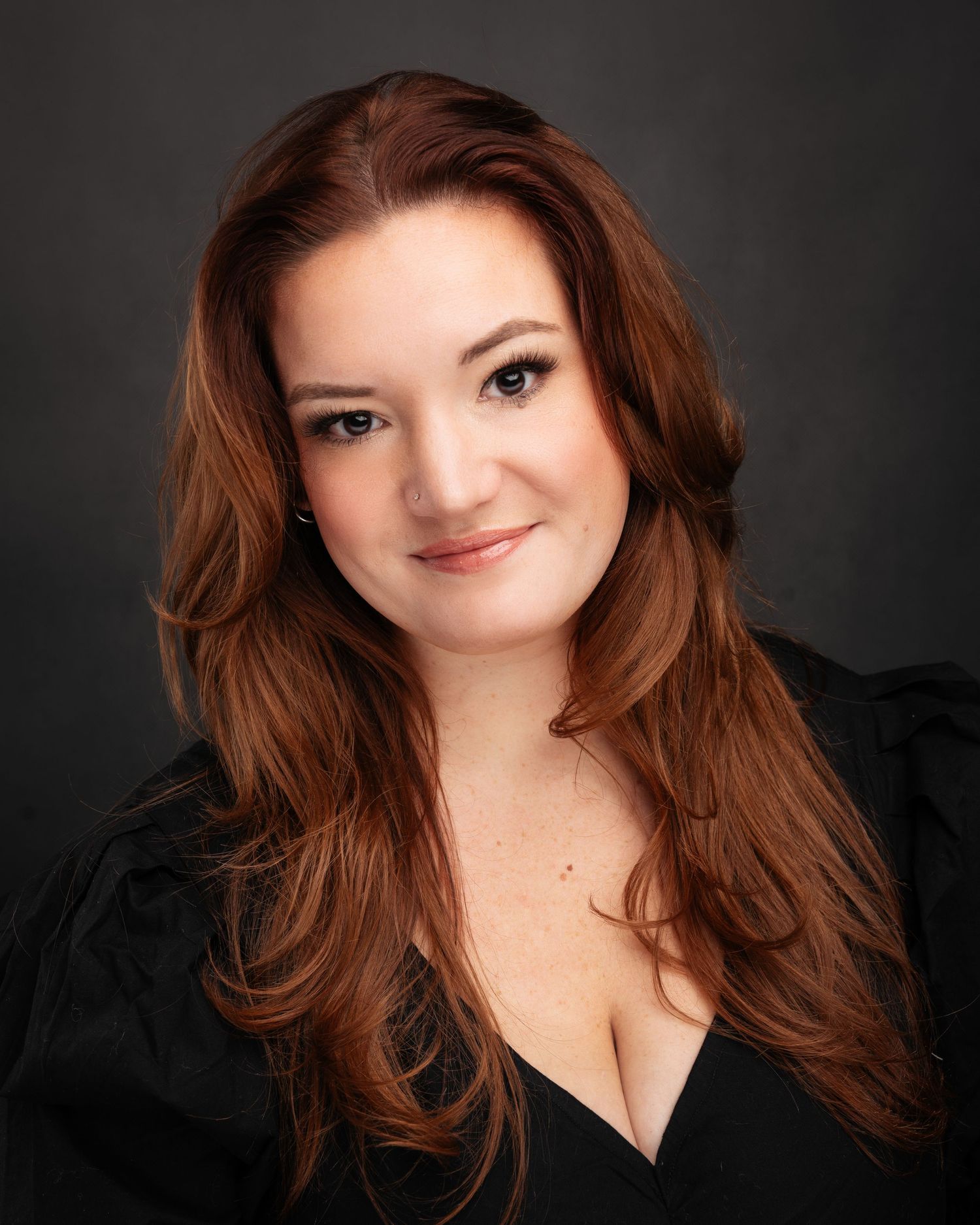 Professional headshots of person with flowing red hair wearing black top.
