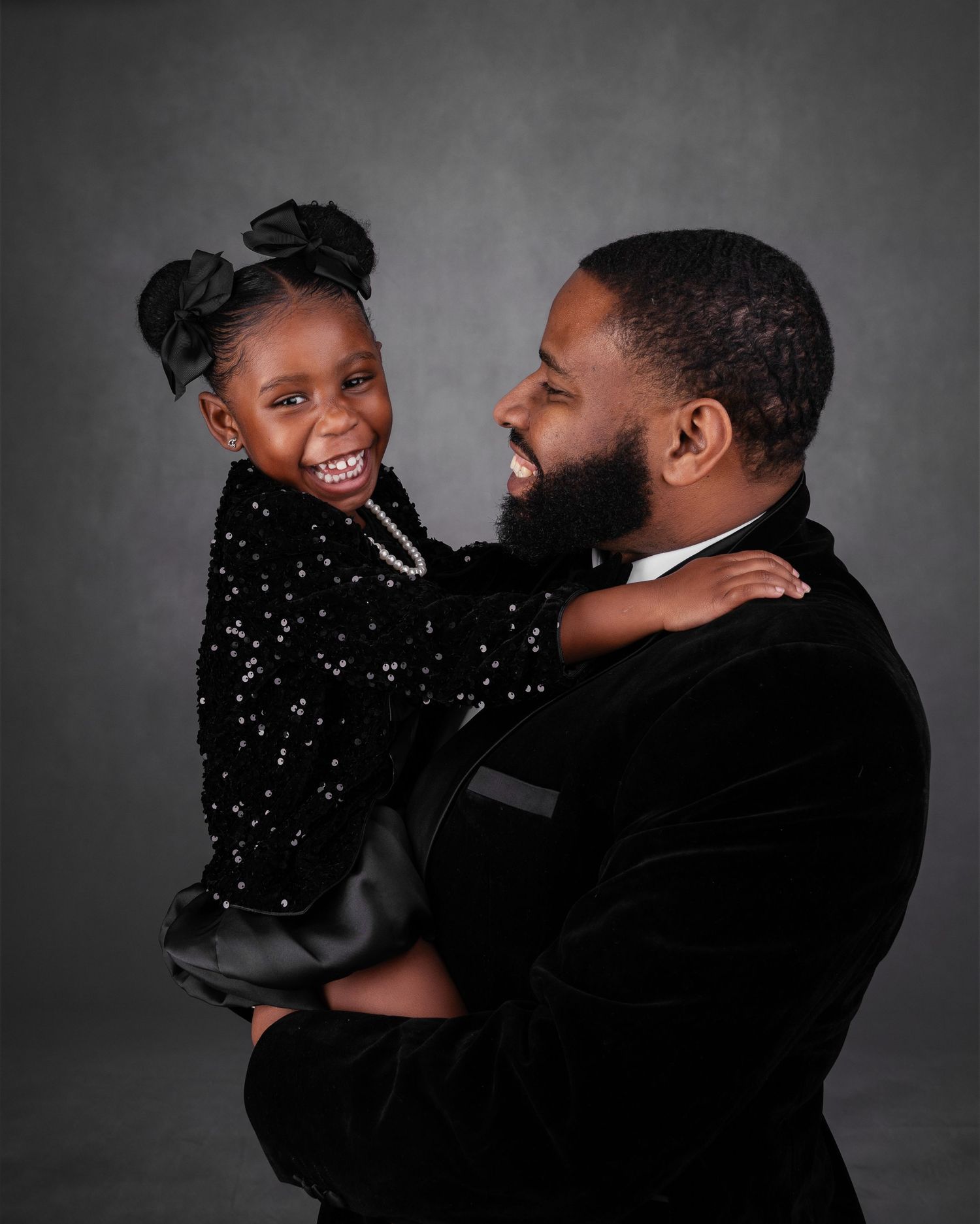 Joyful moment captured between parent and child in formal attire against gray background.
