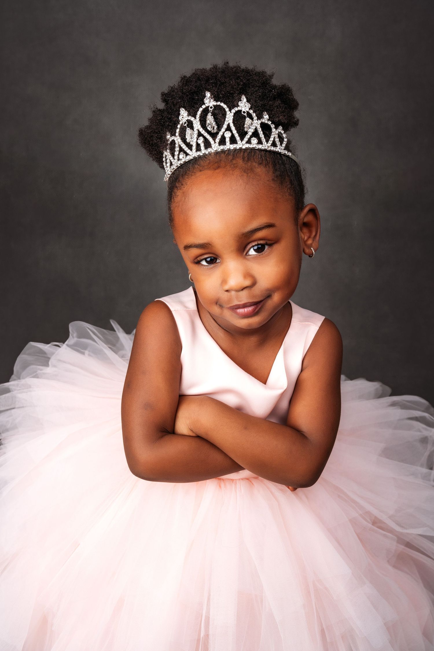 Princess photoshoot featuring white tulle dress and tiara against dark grey backdrop.