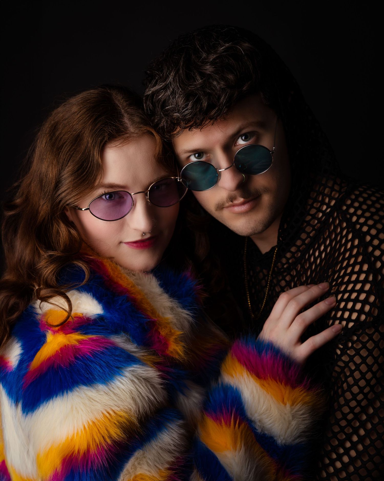 Fashion portrait featuring colorful fur coat and round sunglasses against dark background.