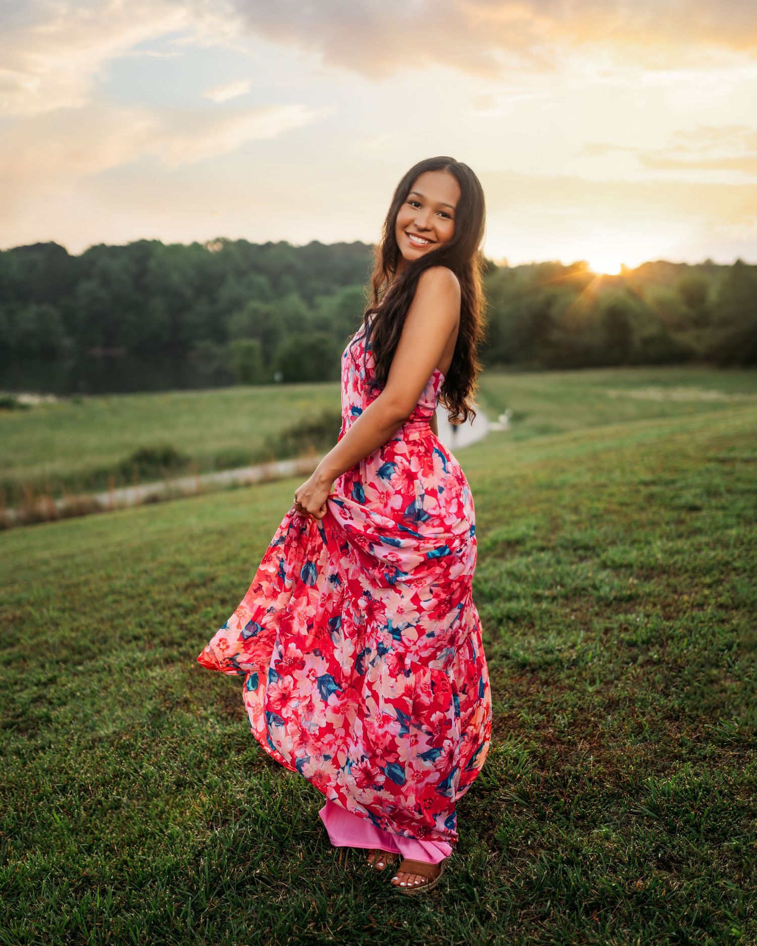 Outdoor portrait session at sunset featuring a flowing red floral dress in a grassy field.