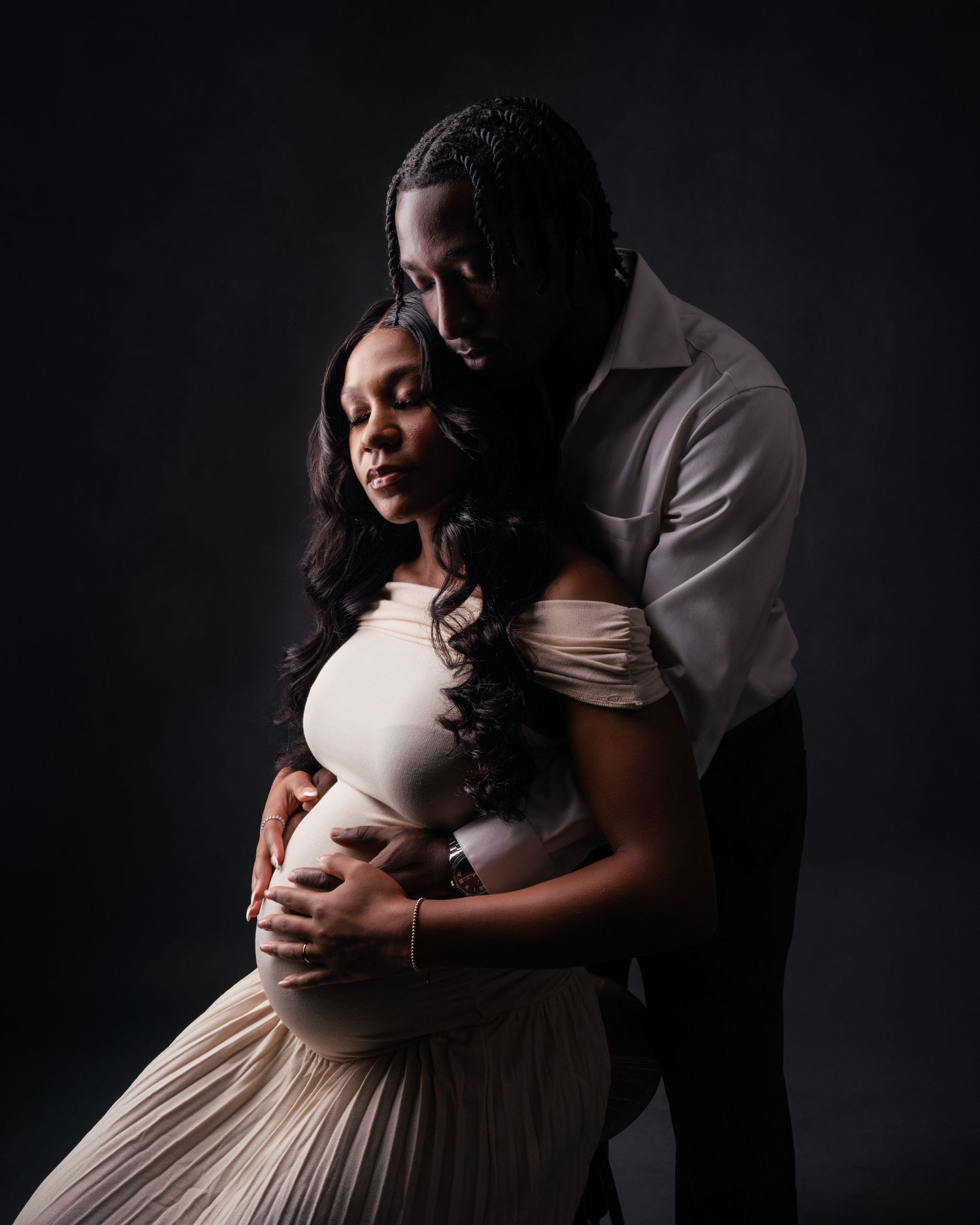 Intimate maternity photography with soft lighting and flowing cream-colored dress.