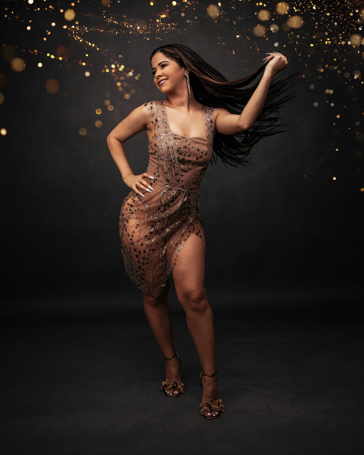 Artistic maternity photoshoot with gold sparkles and a sheer brown dress against dark background.