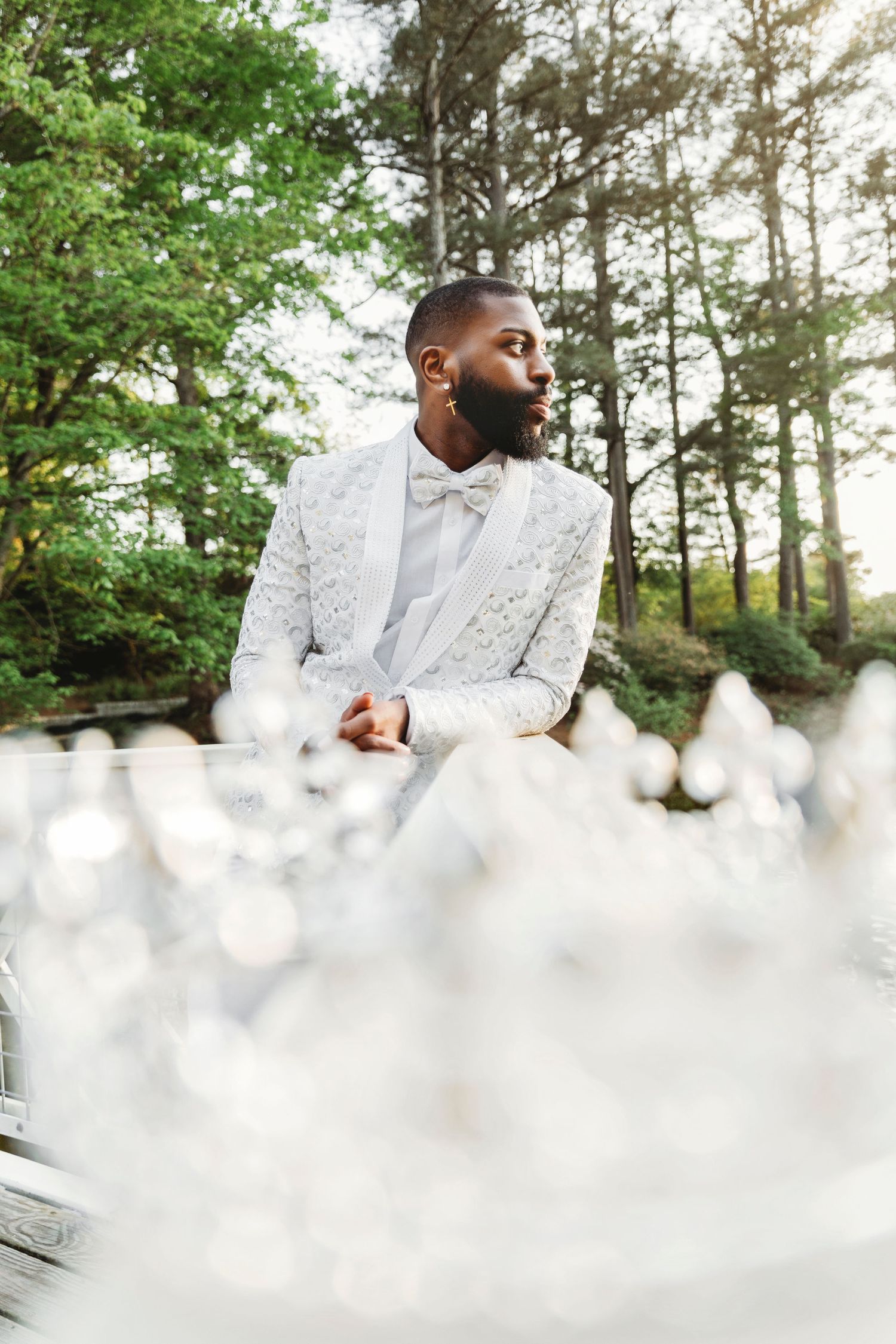 Person in elegant white lace attire poses in wooded outdoor setting with natural lighting.
