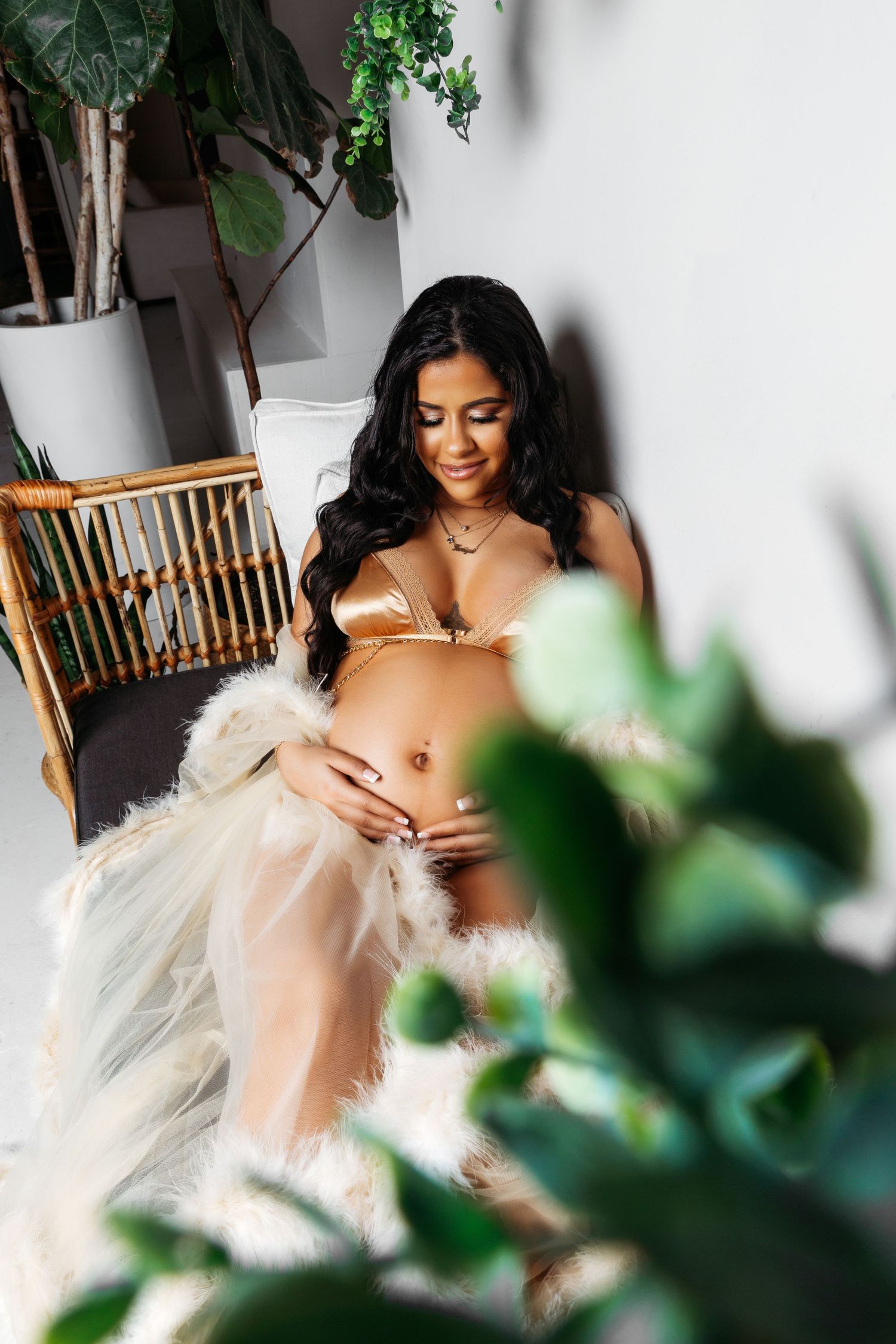 Intimate boudoir photo session with white feather robe and tropical plant accents.