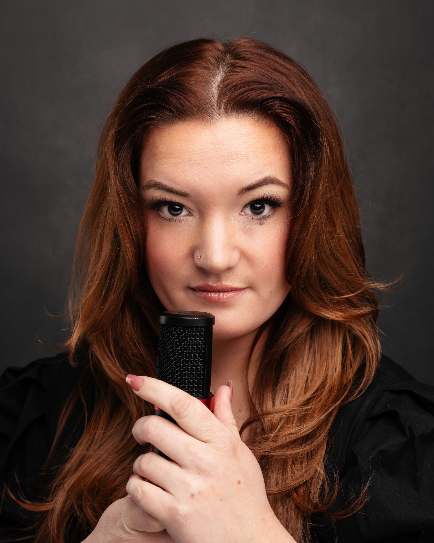 Studio portraits showing person with red hair holding phone against dark background.