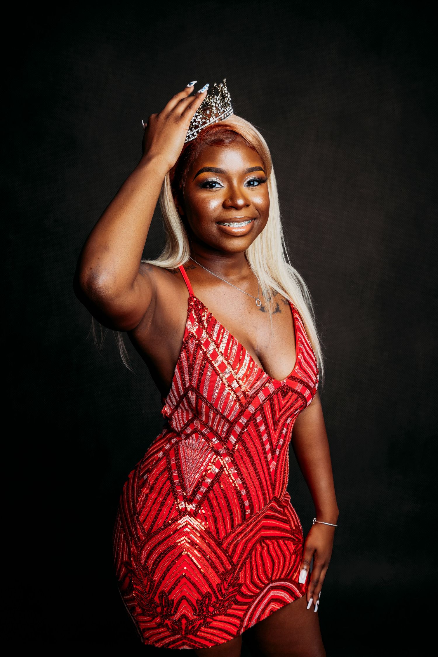 Glamour portrait in sparkly red dress with dramatic lighting against black background.