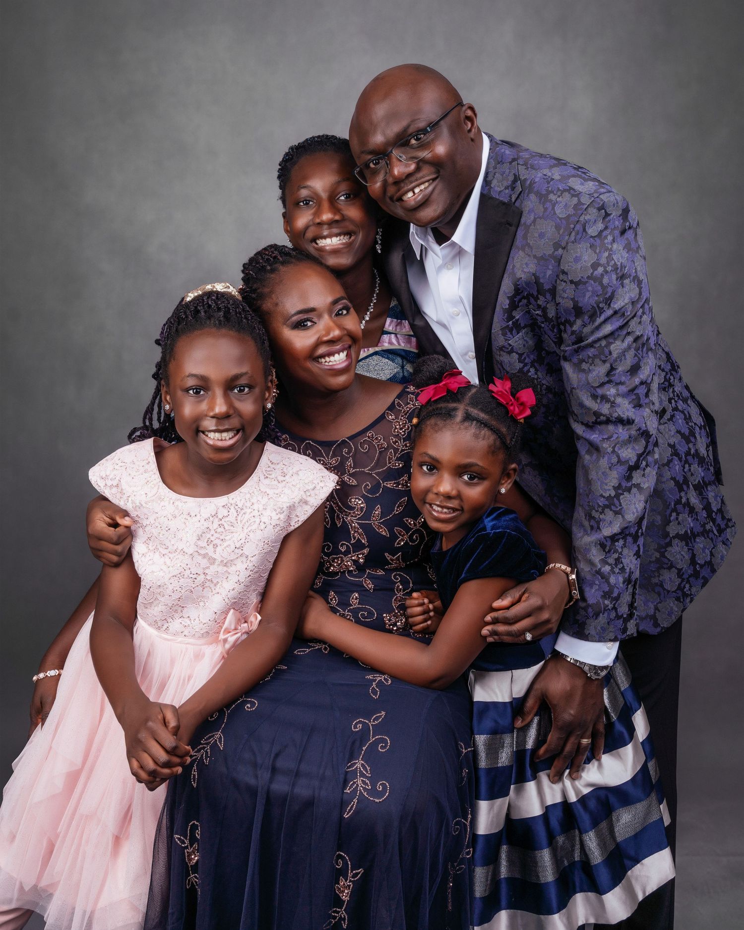 Formal family portrait with coordinated outfits against gray backdrop.