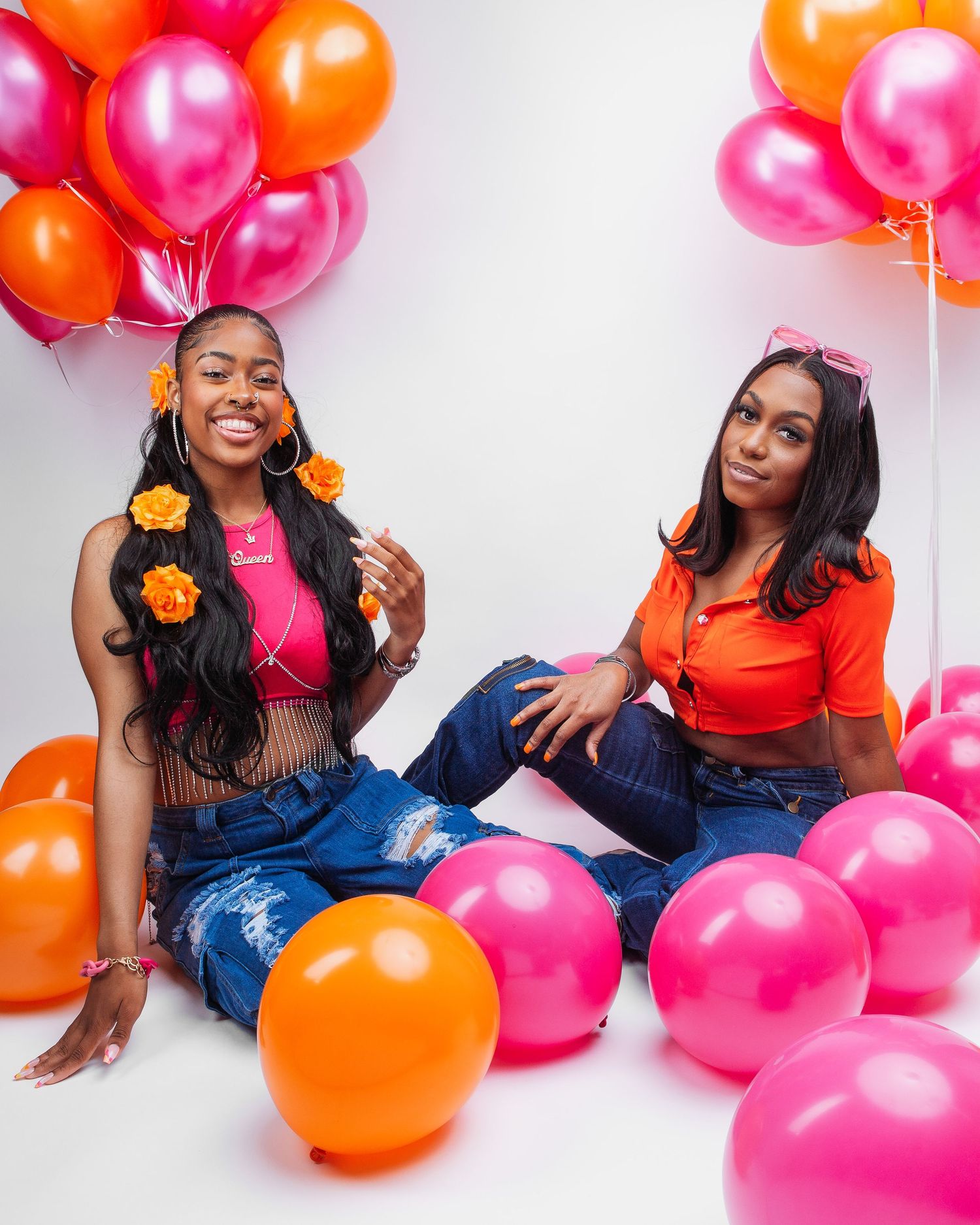 People posing playfully with pink and orange balloons against white background.