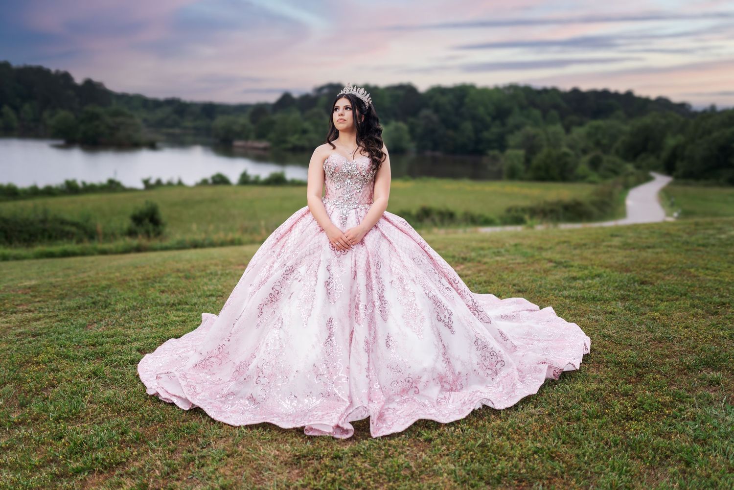 A princess-style pink ball gown with intricate beading photographed in a scenic outdoor setting.