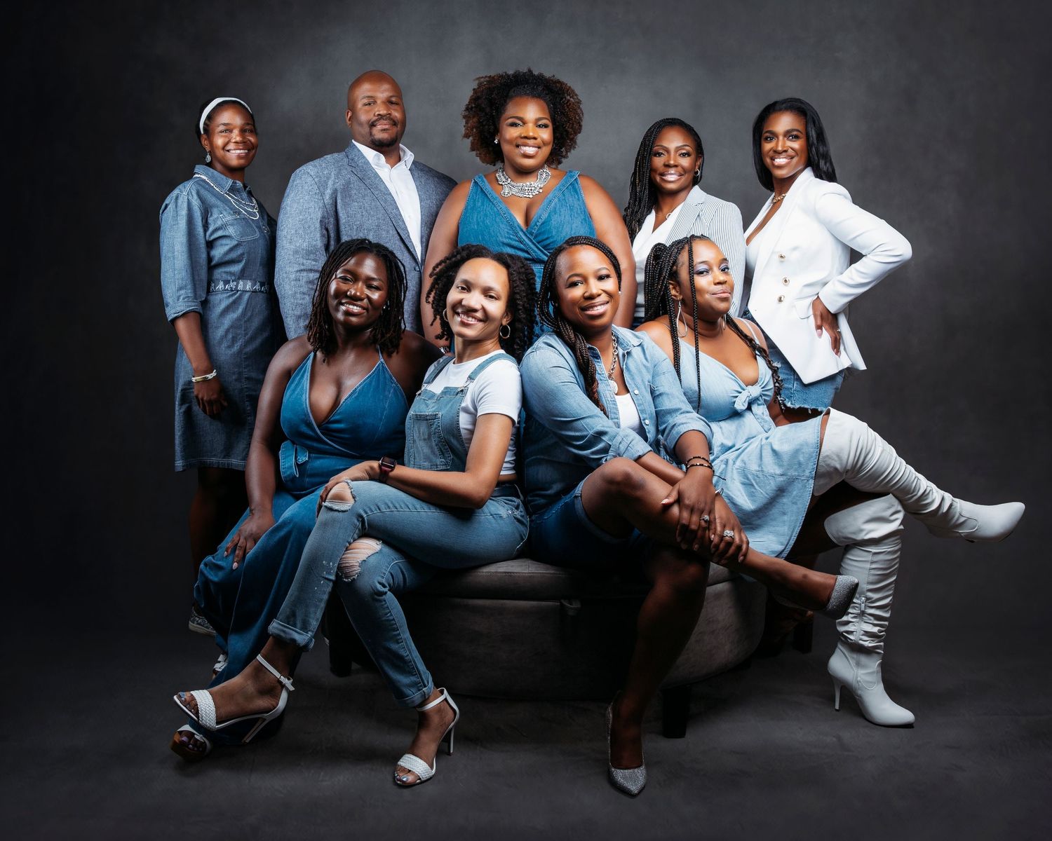 Group photo shoot with coordinated denim and white outfits against dark studio backdrop.