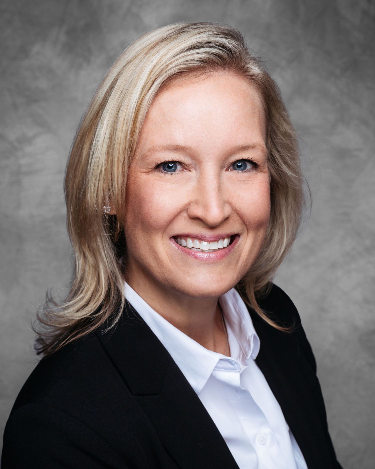Professional headshot of a person in business attire against a gray backdrop.
