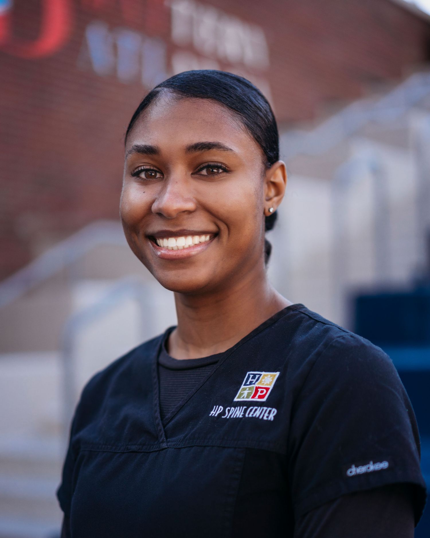 A staff member in a black uniform stands outside a brick building.