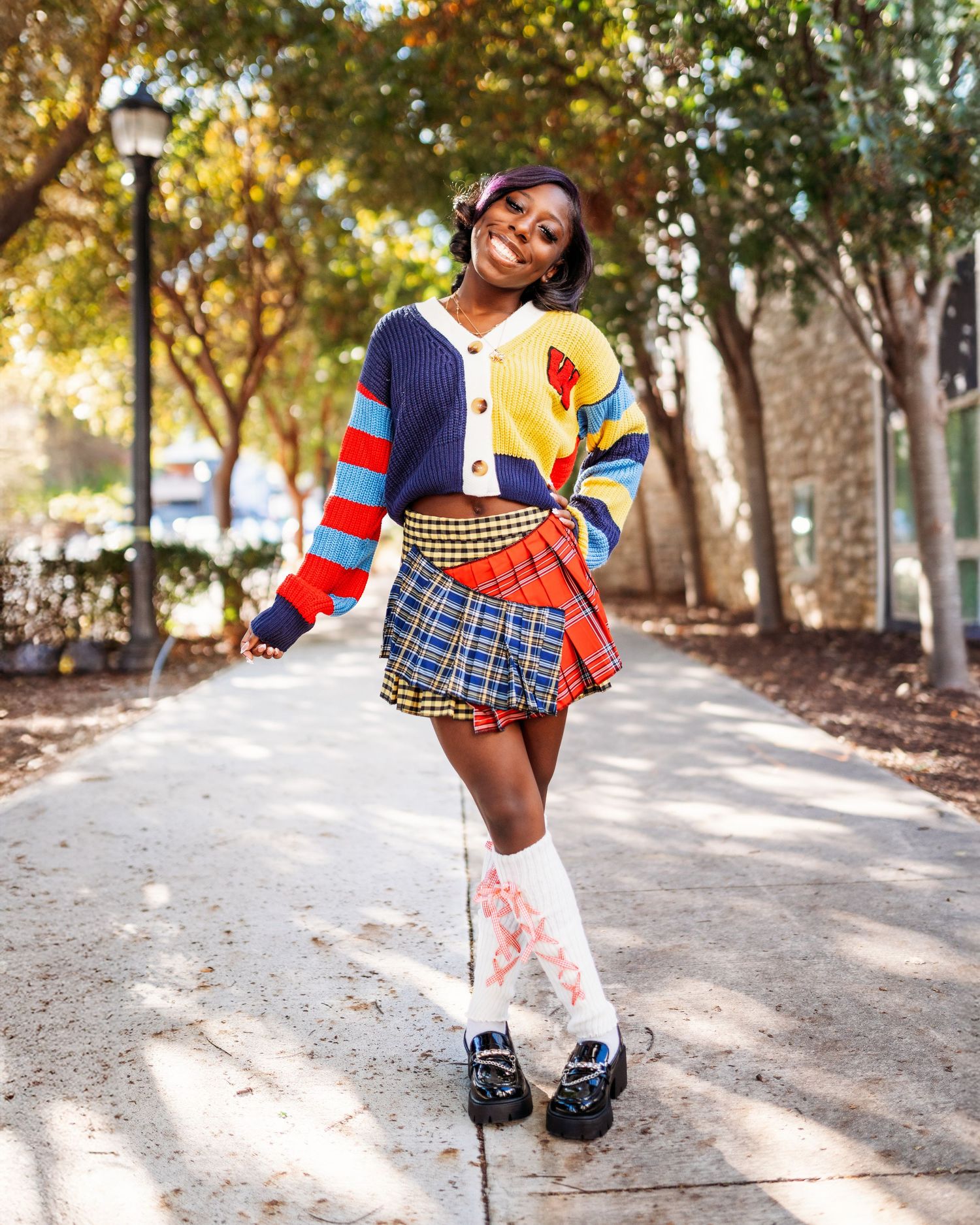 A person in colorful clothing poses playfully on a tree-lined path.