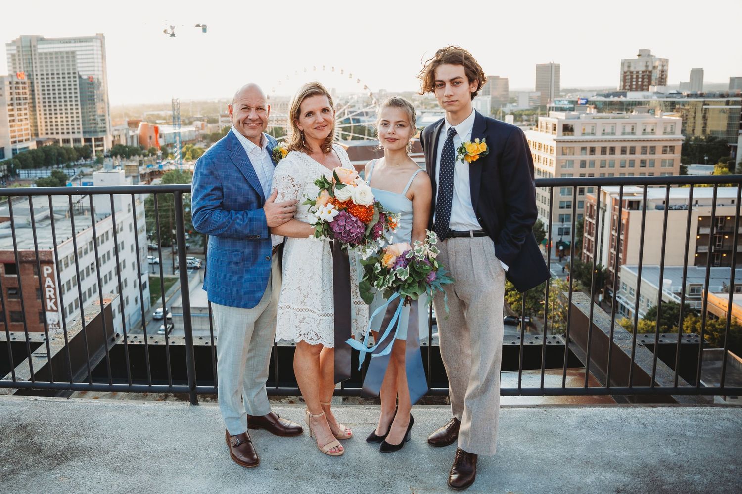 Wedding celebration group photo on a rooftop terrace with city skyline backdrop.