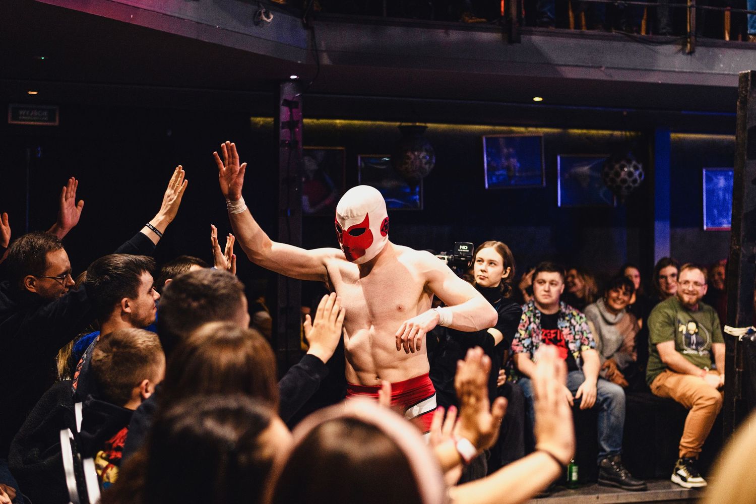 Enthusiastic crowd watching a professional wrestling match in a darkened arena with blue lighting.