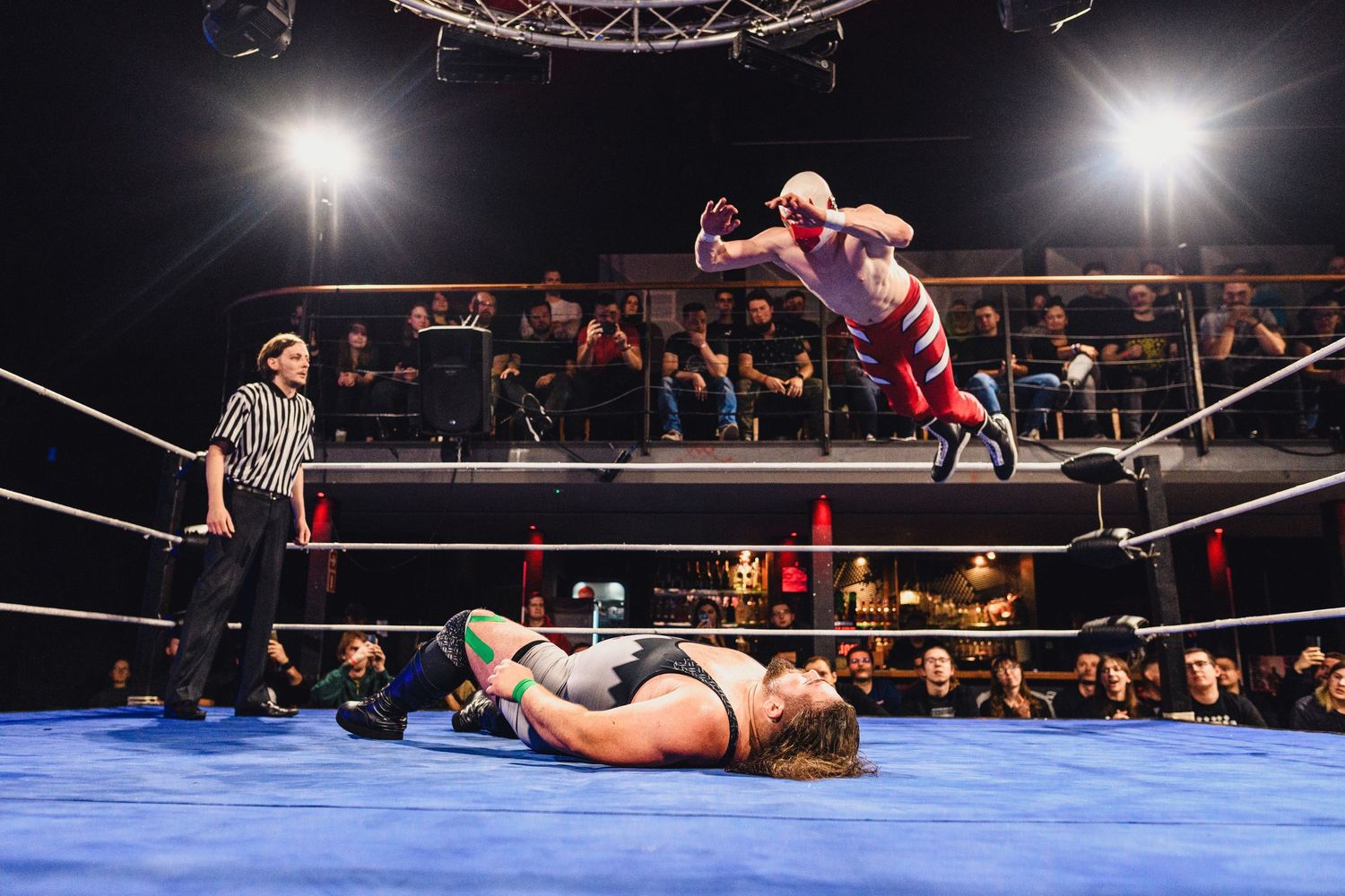 Professional wrestlers compete in an illuminated ring with audience members visible in background.