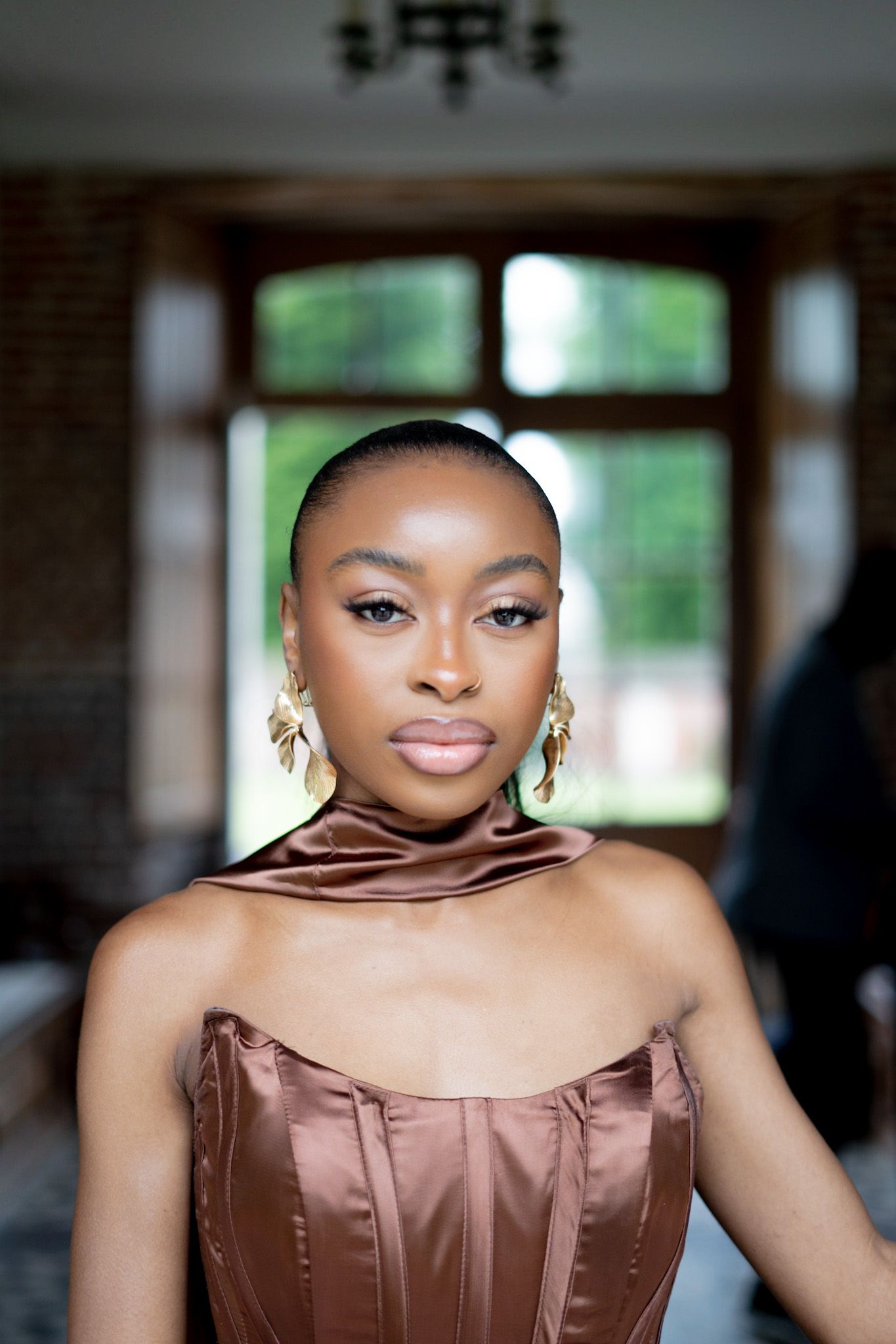 Portrait in brown satin dress with elegant lighting and interior setting.