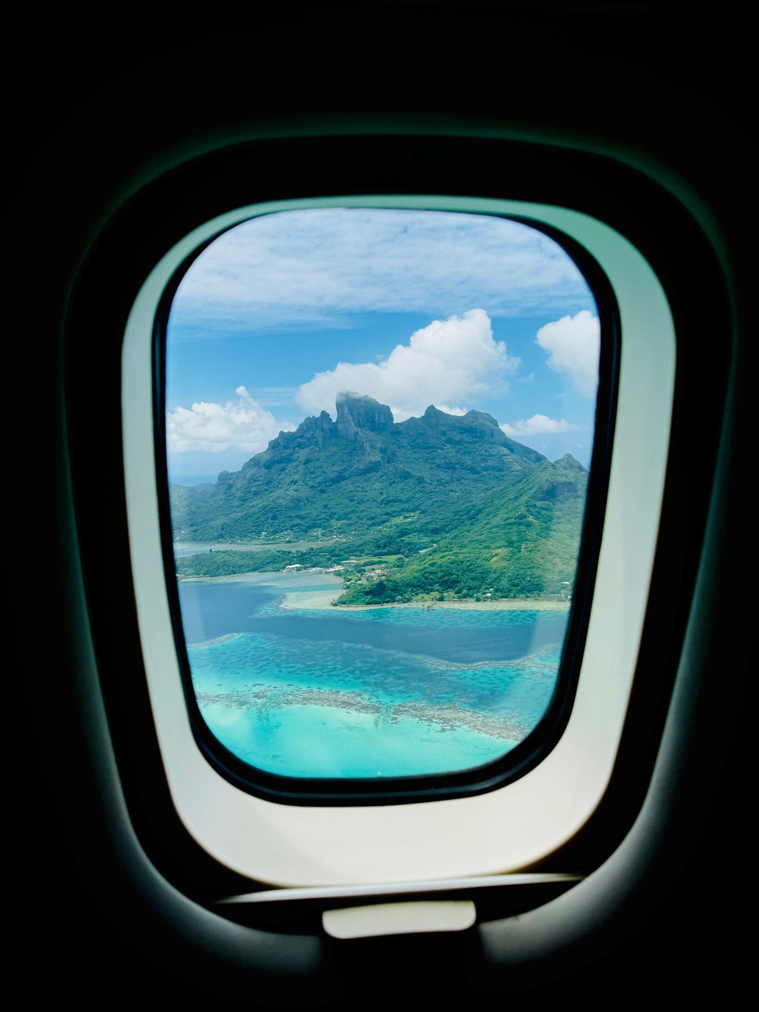 View of a tropical mountain island with turquoise waters and coral reefs through an airplane window in Bora Bora.