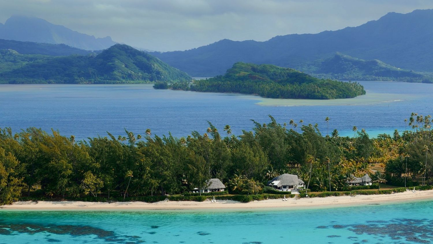 Scenic tropical beach with turquoise waters, mountains and small islands in the background on a sunny day.