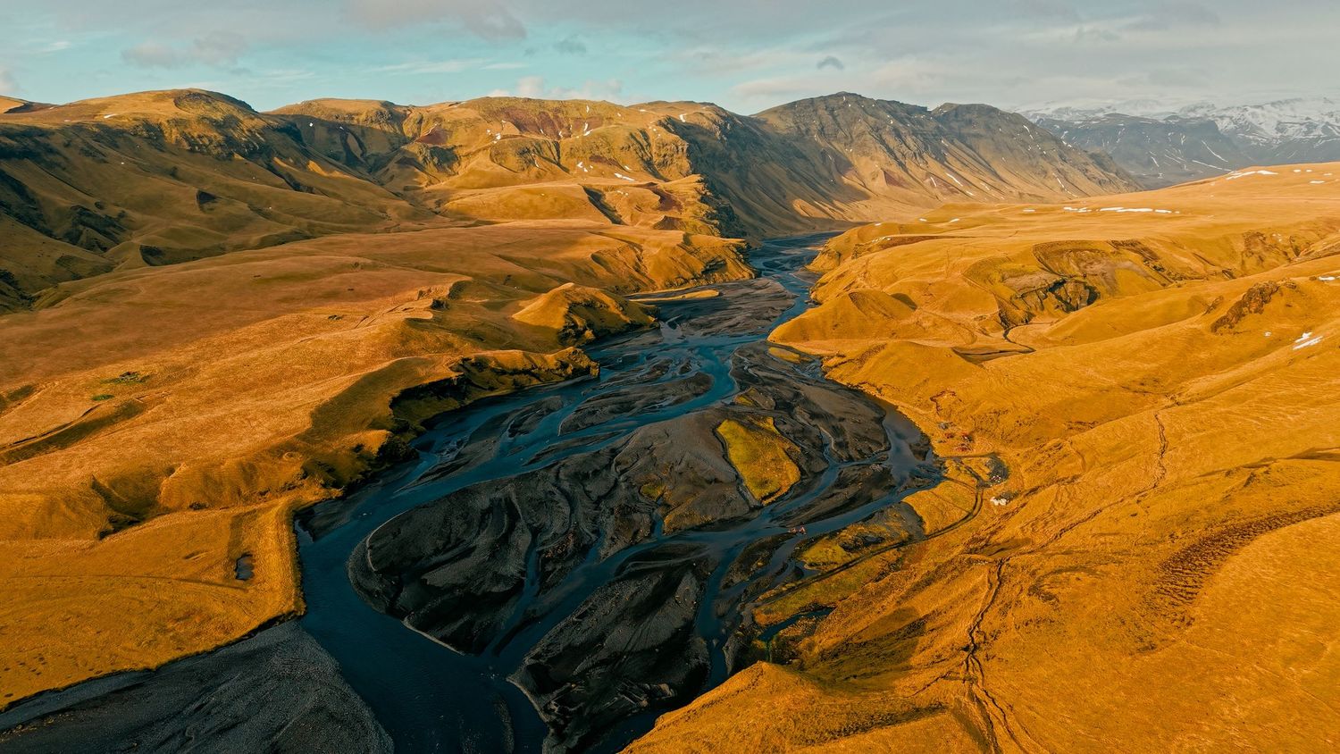 Aerial panoramic view of a winding river cutting through golden hills and mountains during sunset.