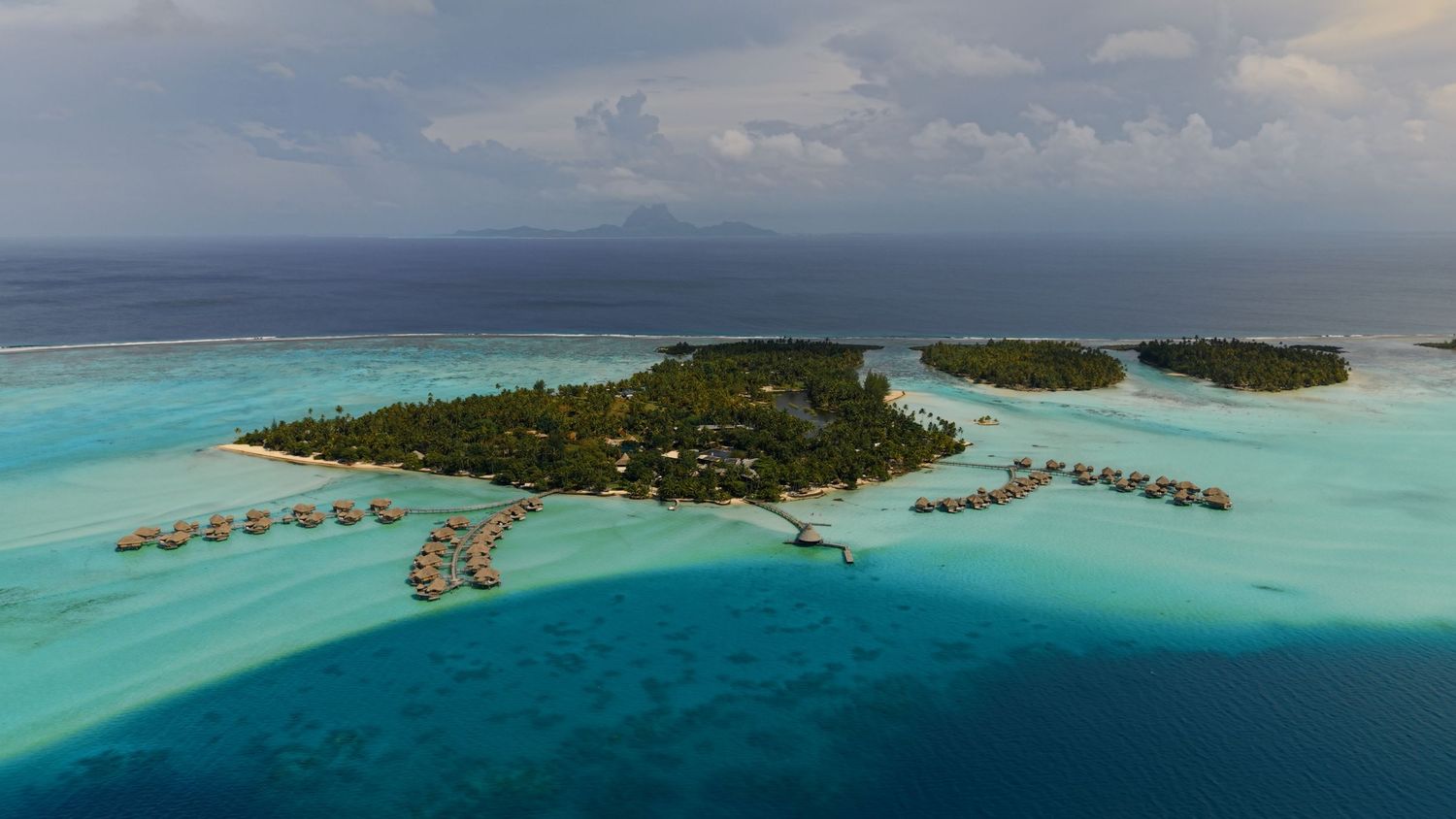 Aerial view of a tropical island resort in the Maldives with overwater bungalows surrounded by turquoise lagoon waters.