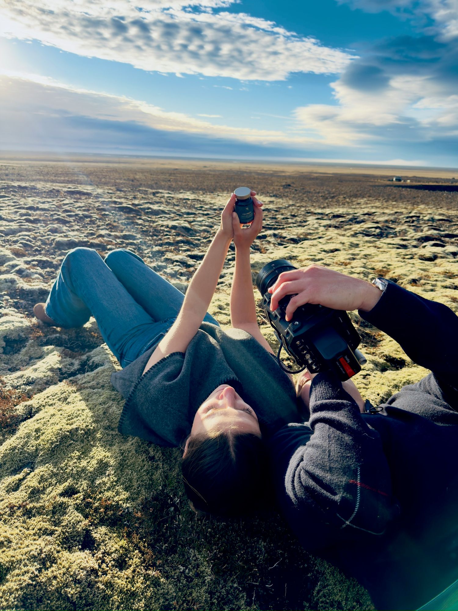 People lying down on mossy ground looking up at a dramatic blue sky with scattered clouds at sunset.