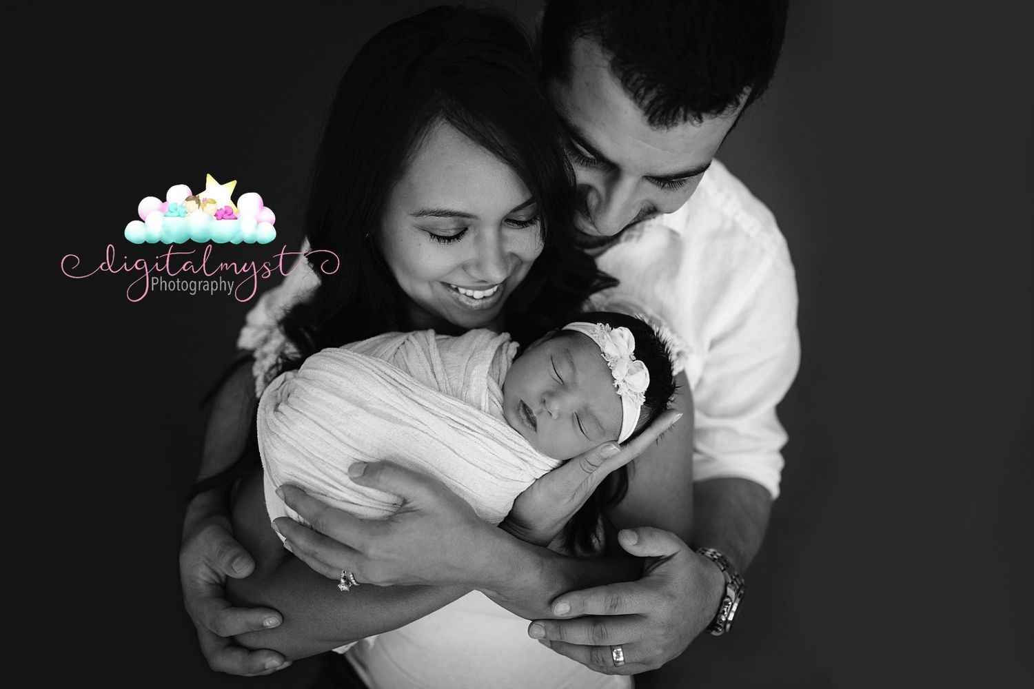 Black and white portrait of parents lovingly holding their newborn baby swaddled in white fabric.