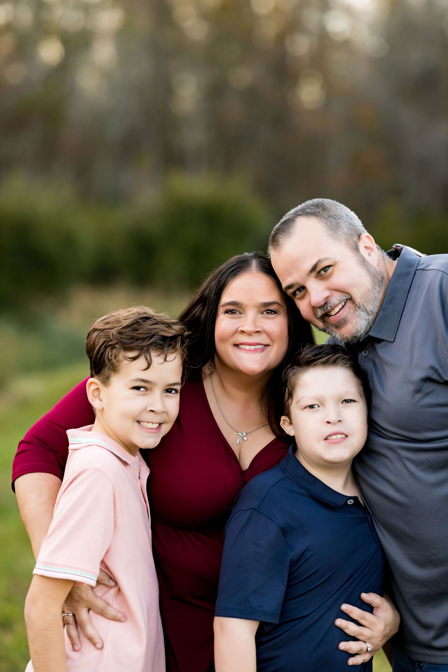 Outdoor family portrait featuring four people in casual attire against blurred natural background.