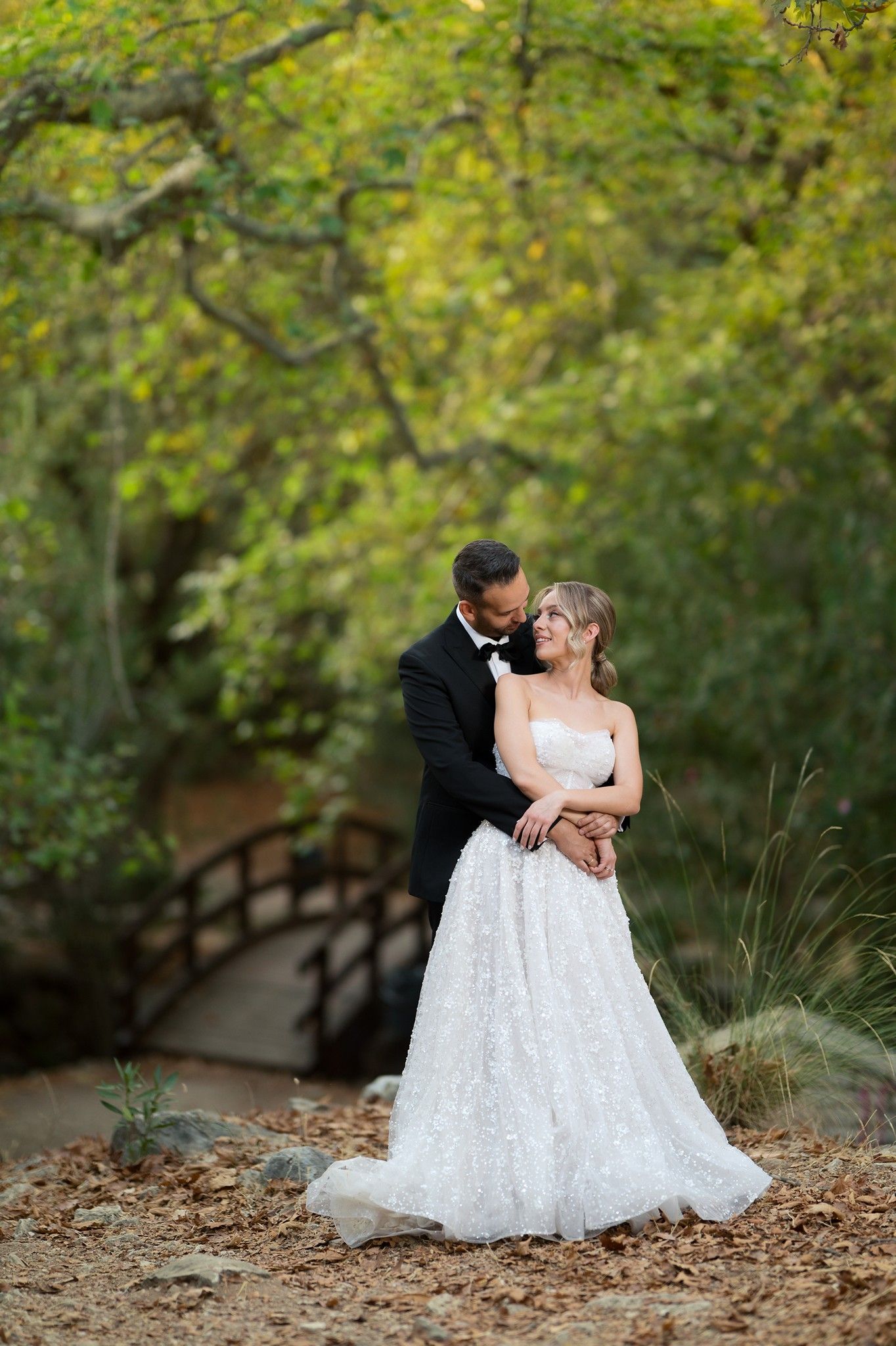 A romantic wedding couple shares intimate moments in a lush garden setting with autumn leaves scattered on the ground.