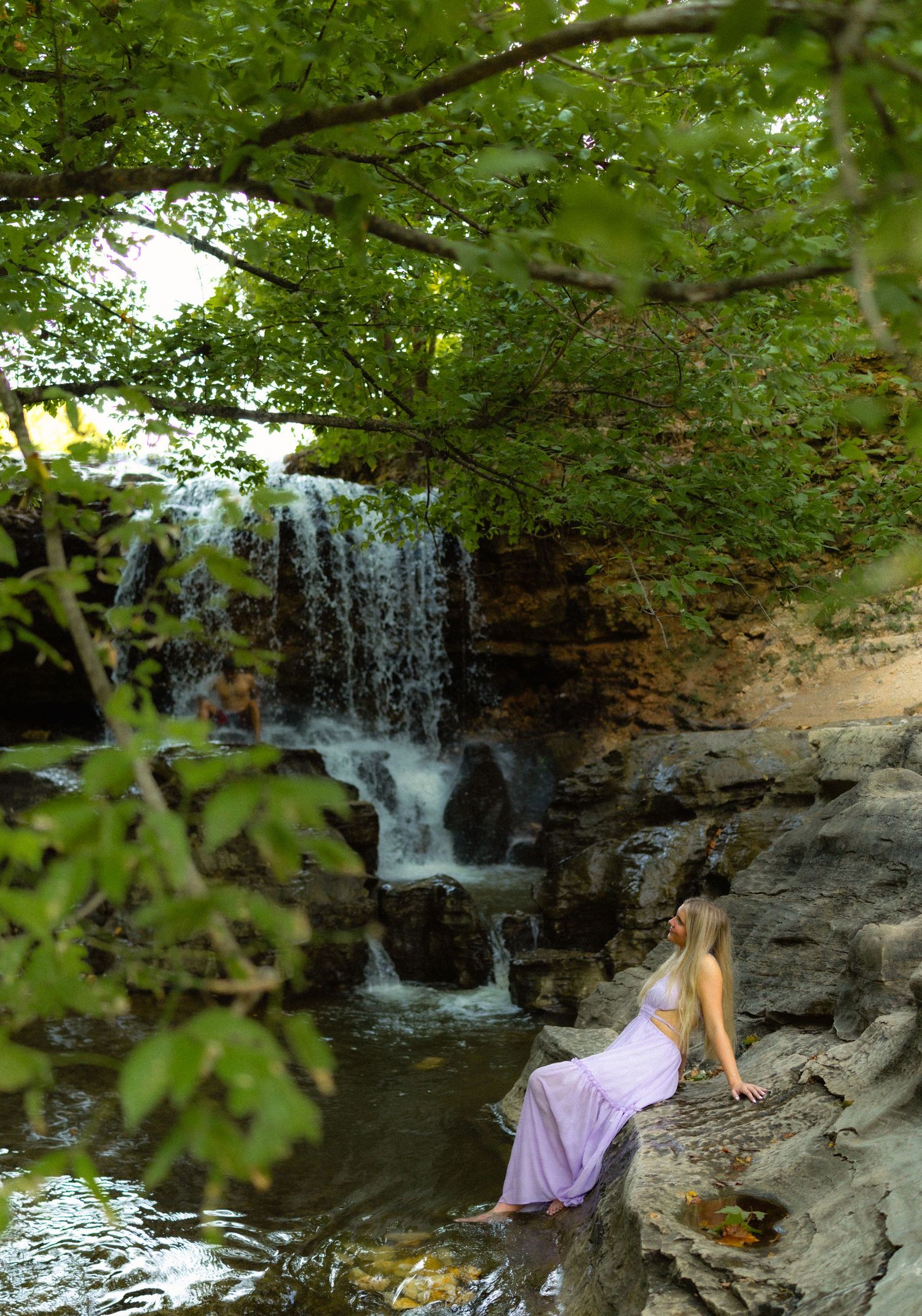 High school senior girl posing by a waterfall during a senior photo session in Bentonville, AR