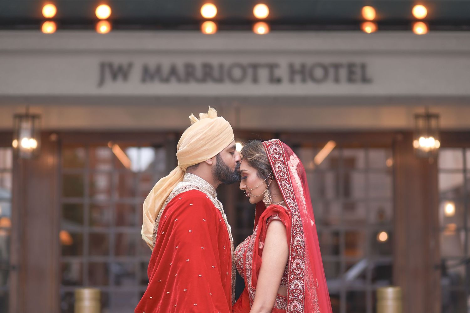 Sikh couple in red wedding attire sharing an intimate moment outside JW Marriott Hotel.