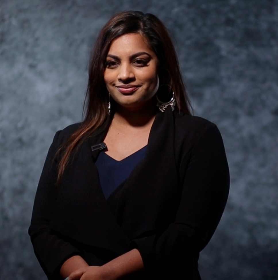 Professional headshot of person in business attire smiling against textured grey background. The Directors Cut Team  Asian Wedding Photograp