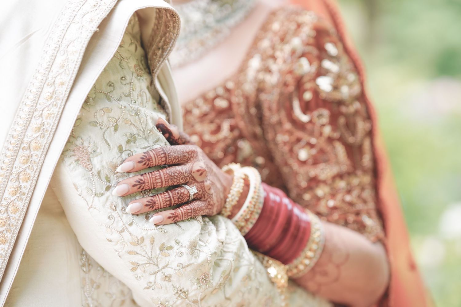 Indian bride's hands adorned with intricate henna and gold bangles holding groom's sherwani.