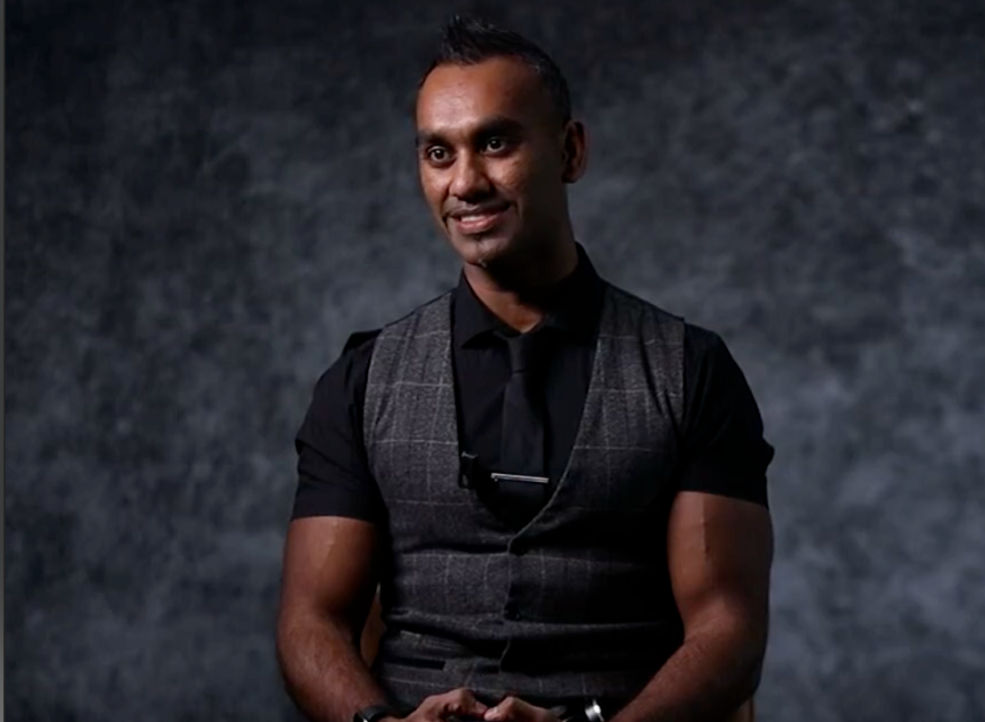 Studio portrait showing person in black shirt and grey vest with warm expression against grey backdrop. The Directors Cut Team