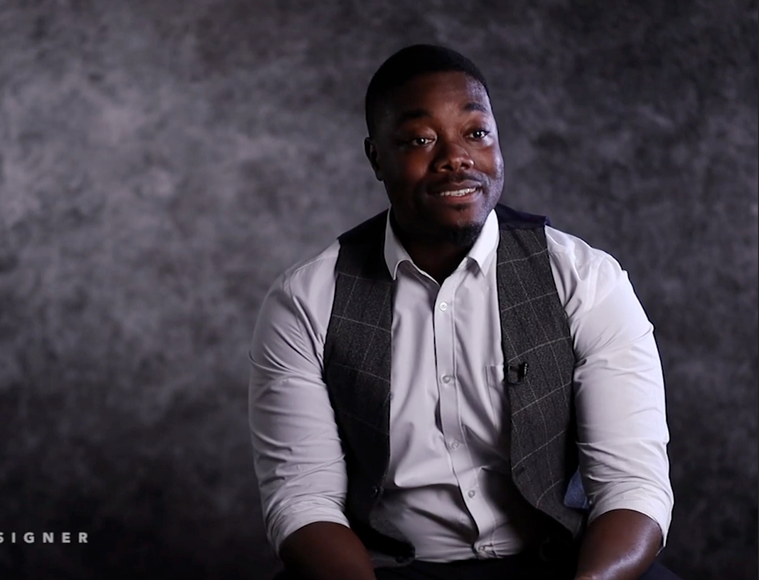 Professional studio portrait of a person wearing a white button-down shirt and gray vest against a dark background.