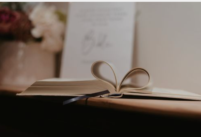 An open Bible with pages spread out on a wooden table, with soft natural lighting creating a cozy reading atmosphere.
