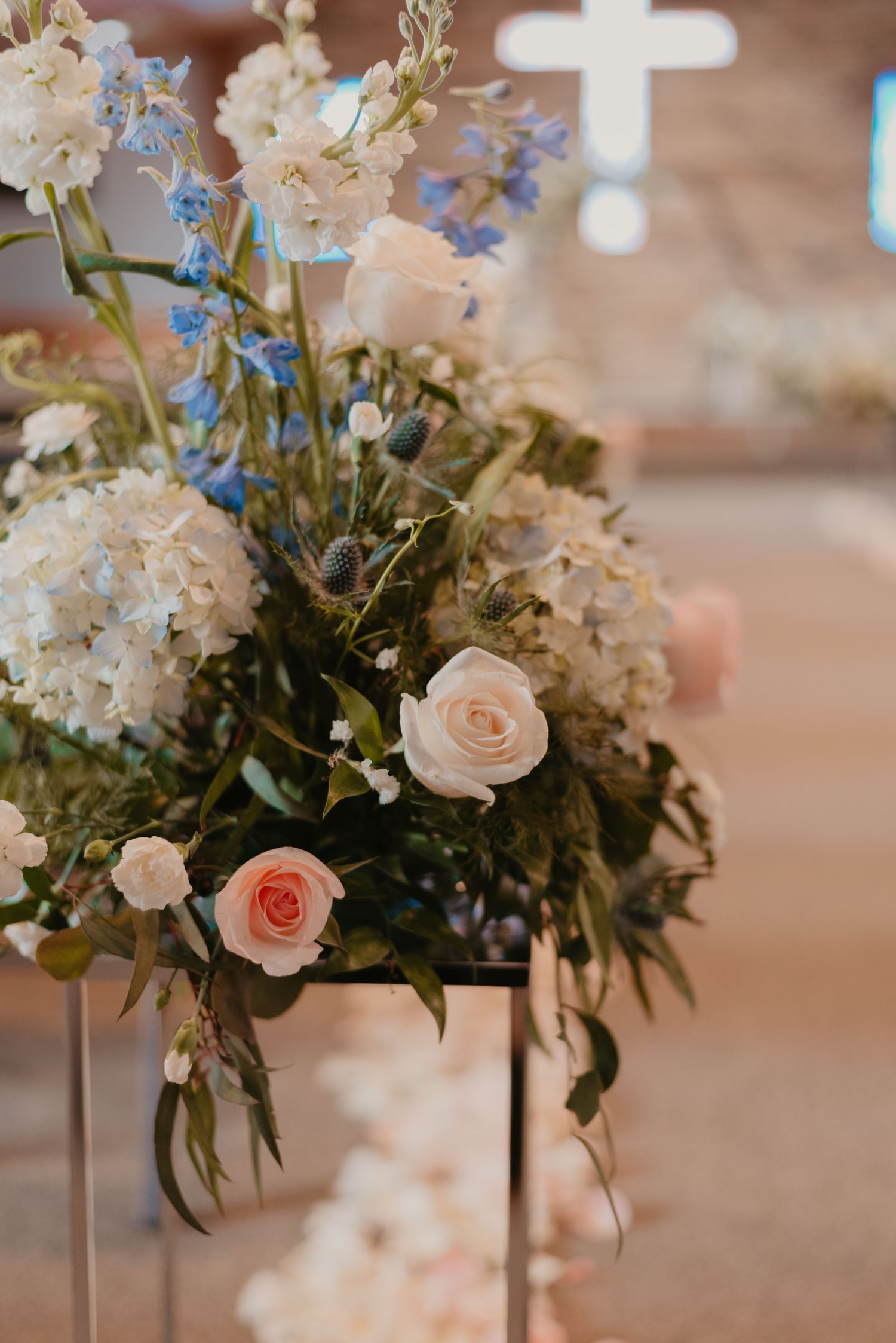 Elegant floral centerpieces featuring blush roses, white blooms, and blue delphinium arranged in tall glass vases.