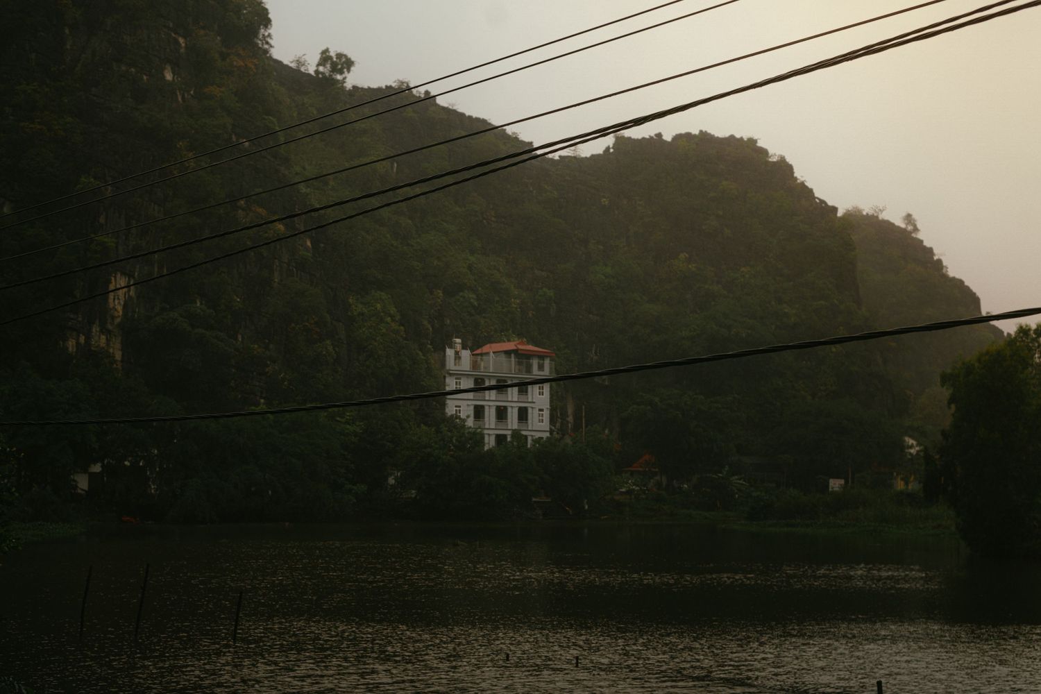 Power lines stretch across a lake with mountains and buildings silhouetted in the dim light.